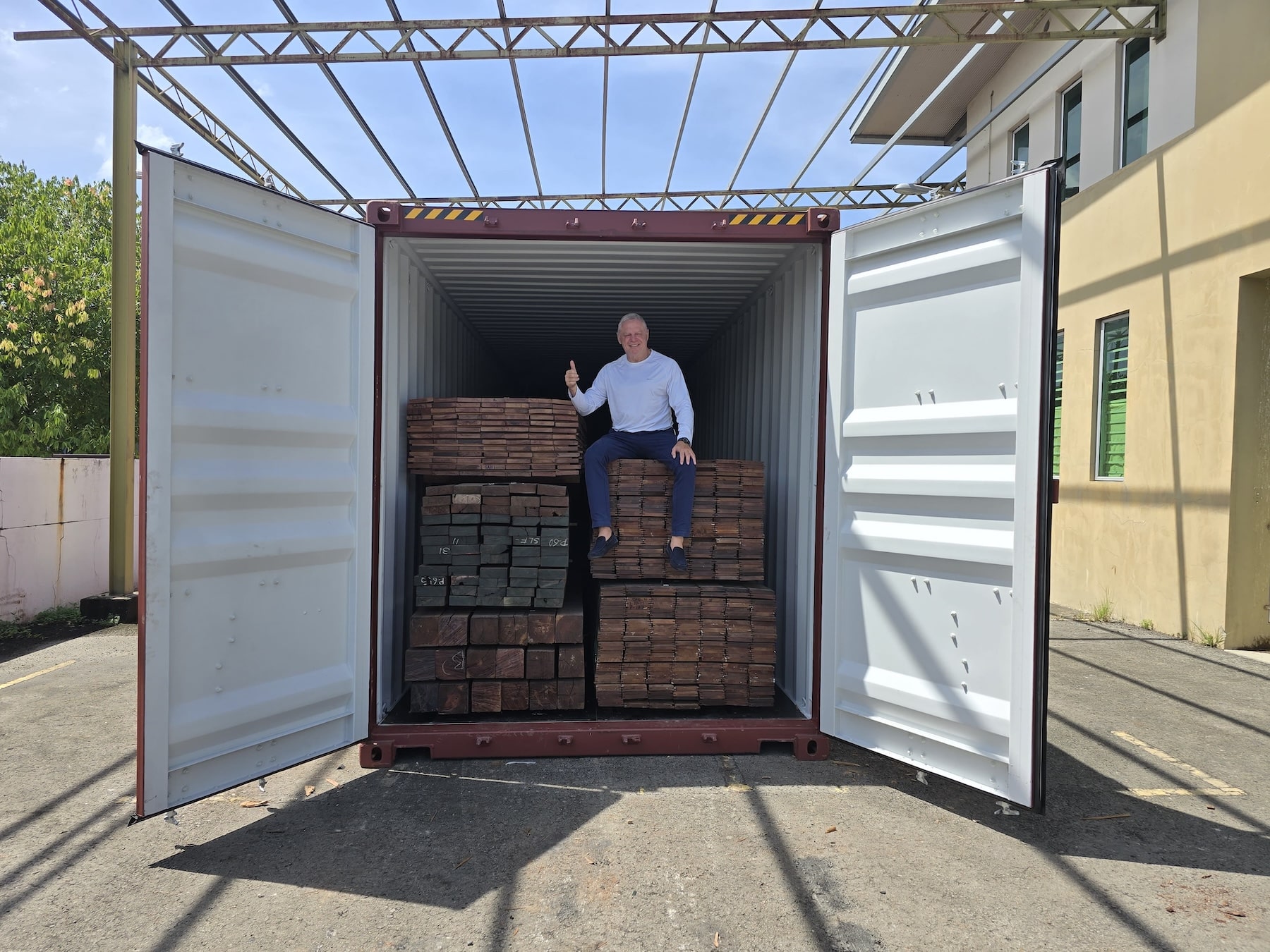 Shipping container with open door and stacks of timber