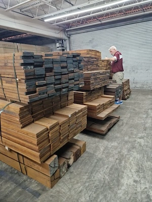 Man inspecting stacks of cut and sorted timber planks in a warehouse with a metal shutter door