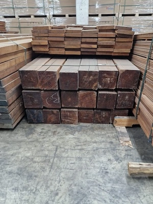 Stacked square timber beams with planed planks on top, stored in a warehouse on a concrete floor