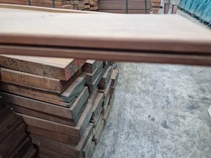 Close-up of a tongue and groove edge on a wooden plank with stacks of timber in the background