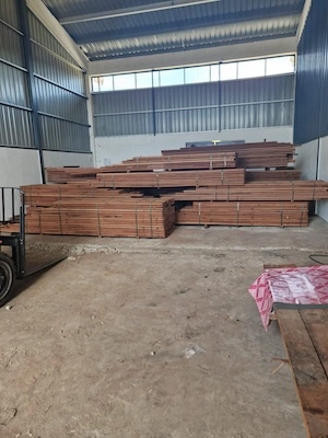 Bundles of sawn timber planks stacked inside a warehouse with high ceilings and metal walls