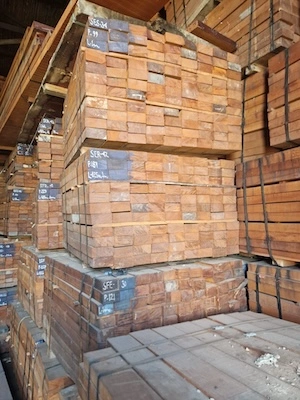 Bundles of sawn timber planks stacked inside a warehouse with high ceilings and metal walls