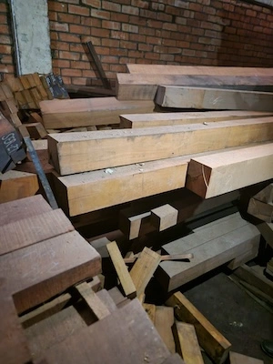 Rough-cut hardwood beams with notches and markings stacked in a warehouse with brick walls