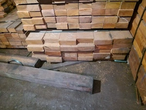 Stacked square-cut timber blocks marked with chalk in a warehouse with sawdust on the floor